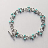 stainless steel bracelet with turquoise beads on a light gray background